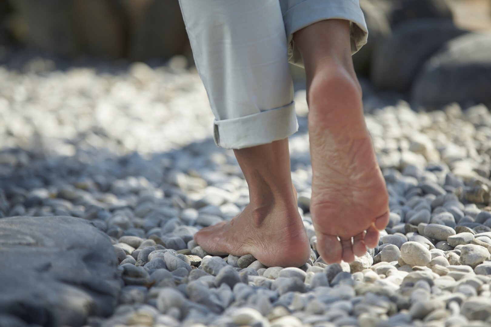 Hier sehen sie Frauenfüße, die Barfuß über größere Kieselsteine gehen. 