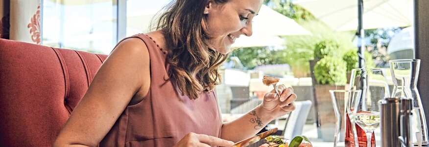 Hier sehen Sie eine Frau mit rosa Oberteil, die eine gesunde Mahlzeit genießt.