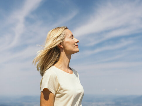 Frau mit geschlossenen Augen vor einem blauen Himmel mit Schleierwolken