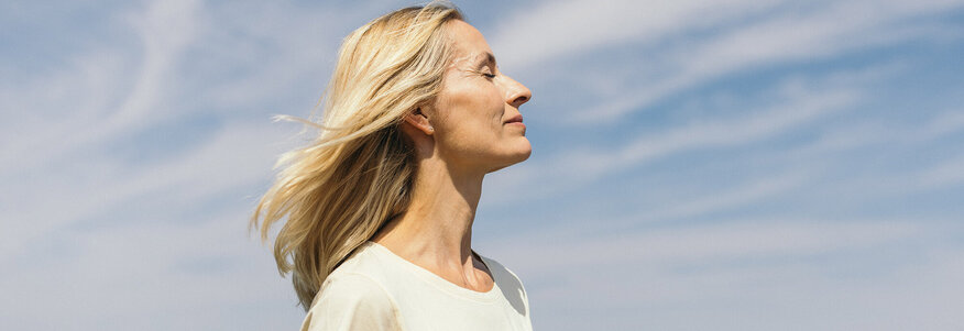 Frau mit geschlossenen Augen vor einem blauen Himmel mit Schleierwolken