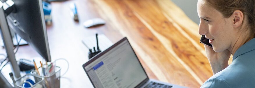 Eine Frau im Homeoffice sitzt an ihrem Schreibtisch vor ihrem Laptop und telefoniert.