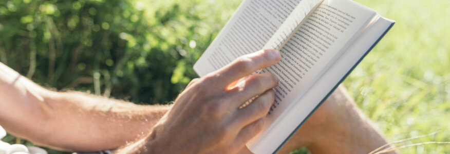 Mann sitzt auf Wiese mit Buch in der Hand