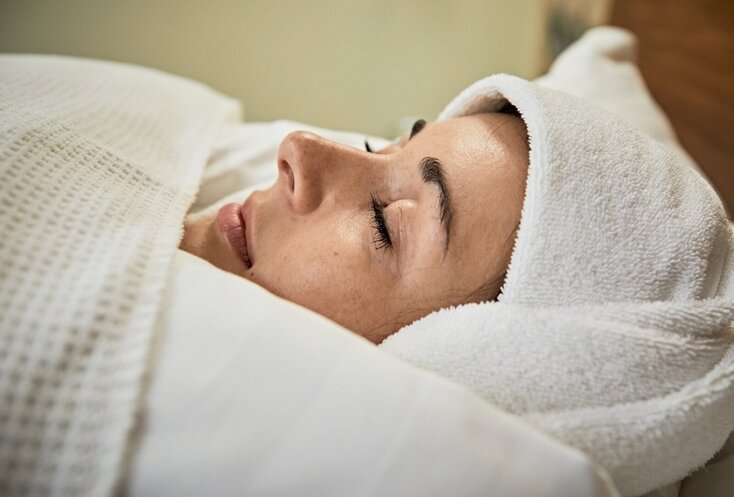 Hier sehen Sie eine Frau, welche in viele Beddecken und Handtücher gewickelt ist. Es ist Teil der Schrothkur. Man sieht in Nahaufnahme ihr Gesicht.