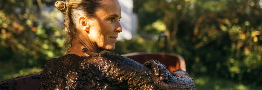 Frau sitzt in einer hölzernen Badewanne bei einer Moorkur