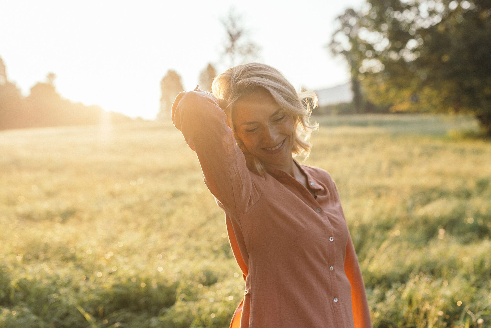 Frau steht auf einer Wiese im Sonnenlicht der Abendsonne