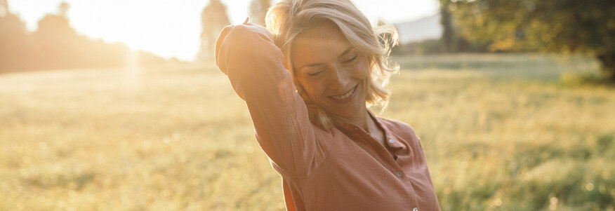 Frau steht auf einer Wiese im Sonnenlicht der Abendsonne