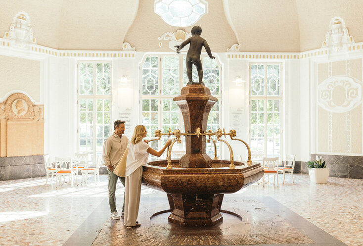 Ein Paar an einem Heilwasser-Trinkbrunnen im bayerischen Staatsbad Bad Kissingen