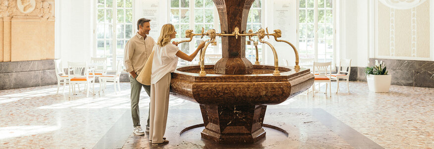 Ein Paar an einem Heilwasser-Trinkbrunnen im bayerischen Staatsbad Bad Kissingen