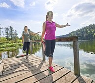 Gesundes Bayern - zwei Frauen machen Stretchübungen auf Steg nahe wunderschönem See, sonniges Wetter