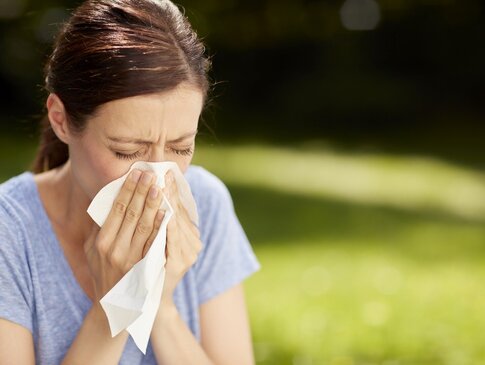 Gesundes Bayern - Frau schnäuzt in Taschentuch im Grünen aufgrund von Allergien