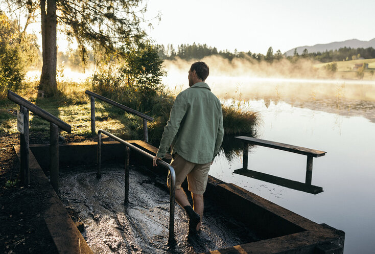 Mann geht durch eine Tröge mit Moor, bei einer Mooranwendung am Wasser
