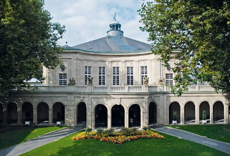 Im Vordergrund ist eine Rasenfläche mit einem bunten Blumenbeet darauf 