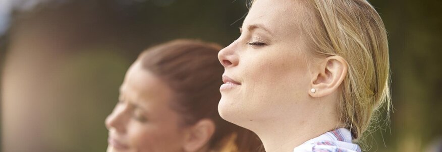 Nahaufnahme von zwei Frauen, die in einer Wiese sitzen und tief durchatmen.