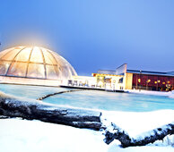 Sie sehen den Außenbereich der Frankentherme. Beleuchtete Kuppe und Schnee drumherum.