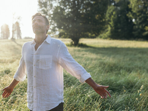 Mann steht in der Morgensonne auf einem Feld und genießt