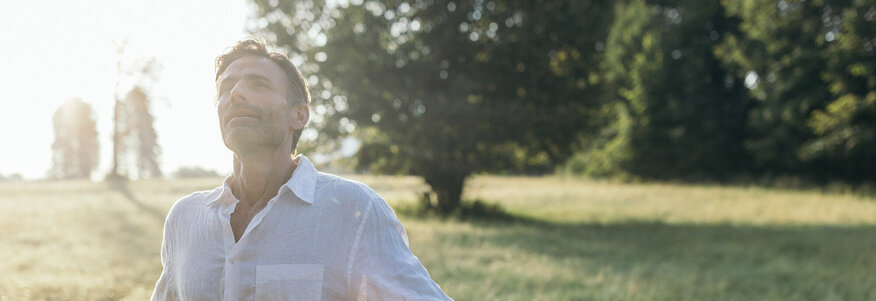 Mann steht in der Morgensonne auf einem Feld und genießt